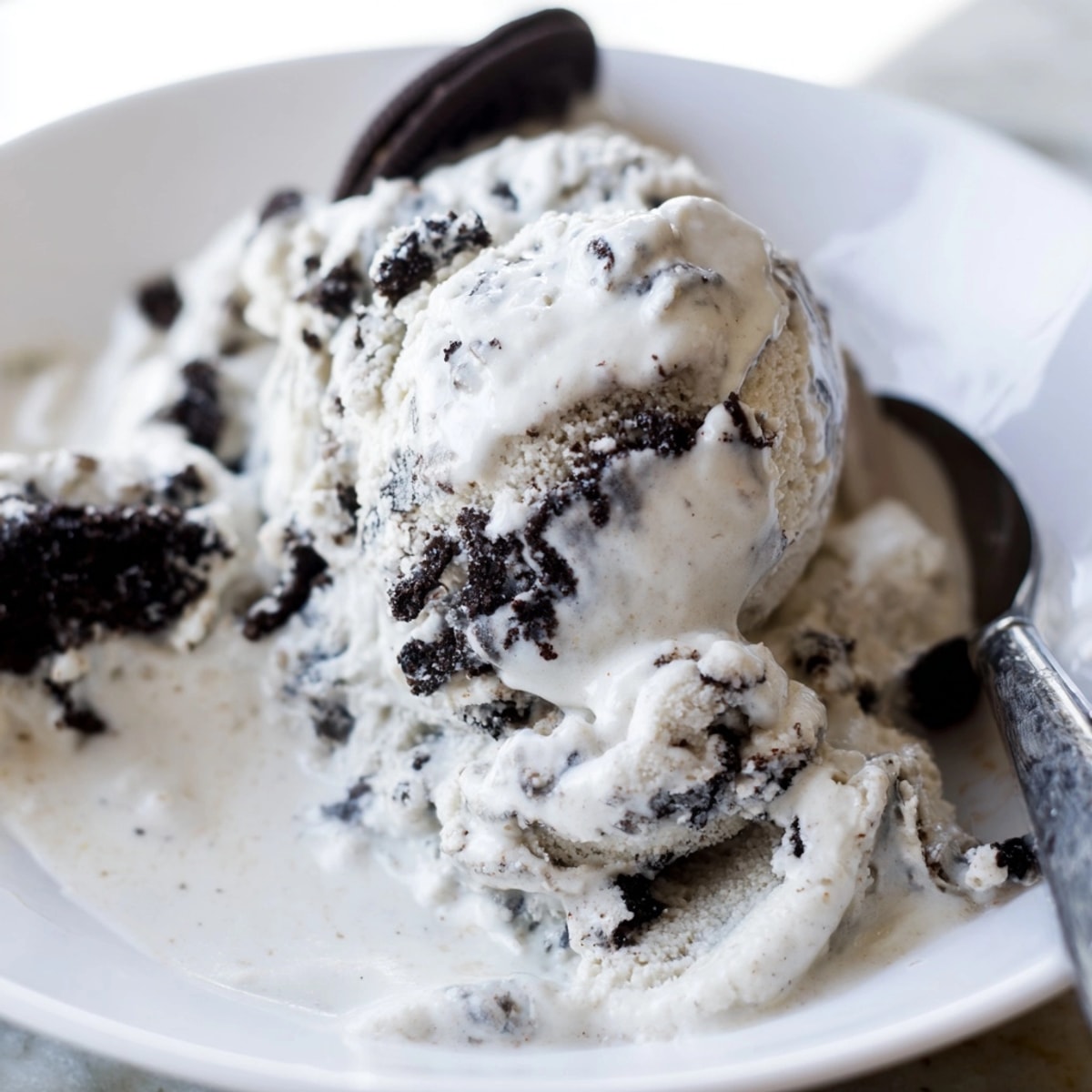 Creamy, sweet Cookies and Cream Ice Cream swirled with chocolate cookie pieces, freezing in a container.