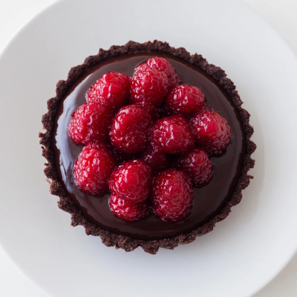 A slice of chocolate raspberry tart showcases fresh, vibrant raspberries atop rich, dark ganache.