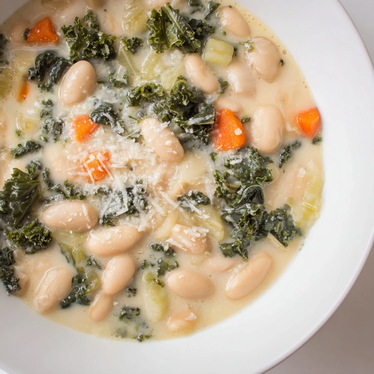 Steaming creamy white bean and kale soup, garnished with Parmesan, inviting you in for a taste.