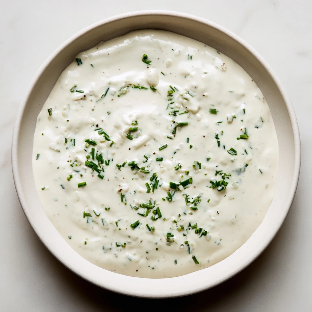 A close-up shot of Creamy Dressing, showcasing a thick, white texture with visible herbs.