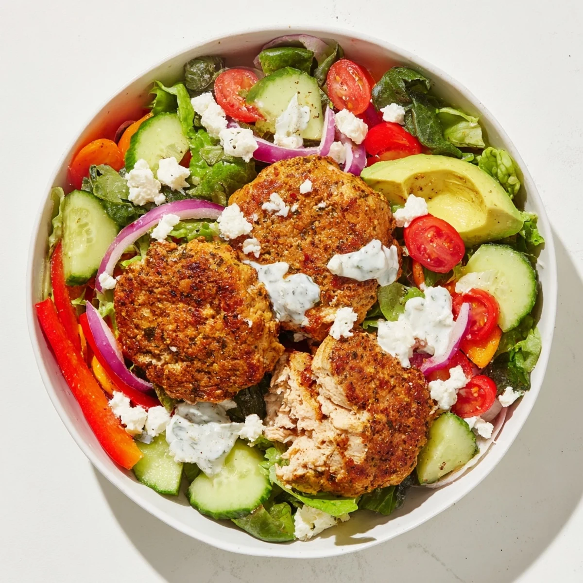 Juicy turkey burger patties atop a fresh salad bowl with creamy yogurt dressing, a delicious meal.