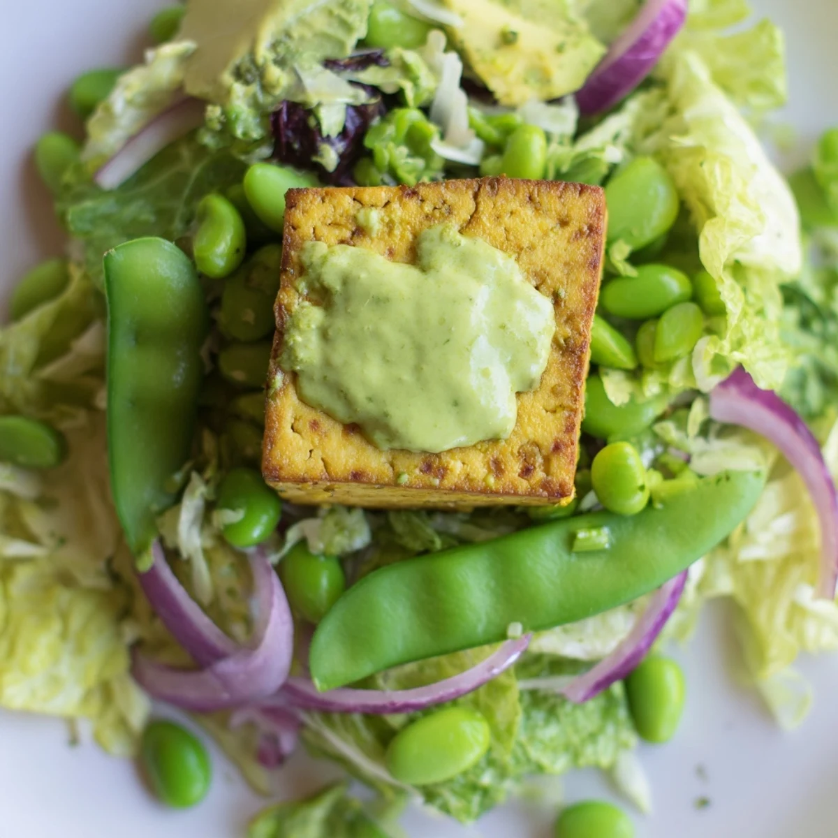 A close-up of the Green Goddess Salad with Baked Tofu, showing crispy golden tofu cubes nestled in crisp romaine lettuce, shredded cabbage, and bright green edamame.