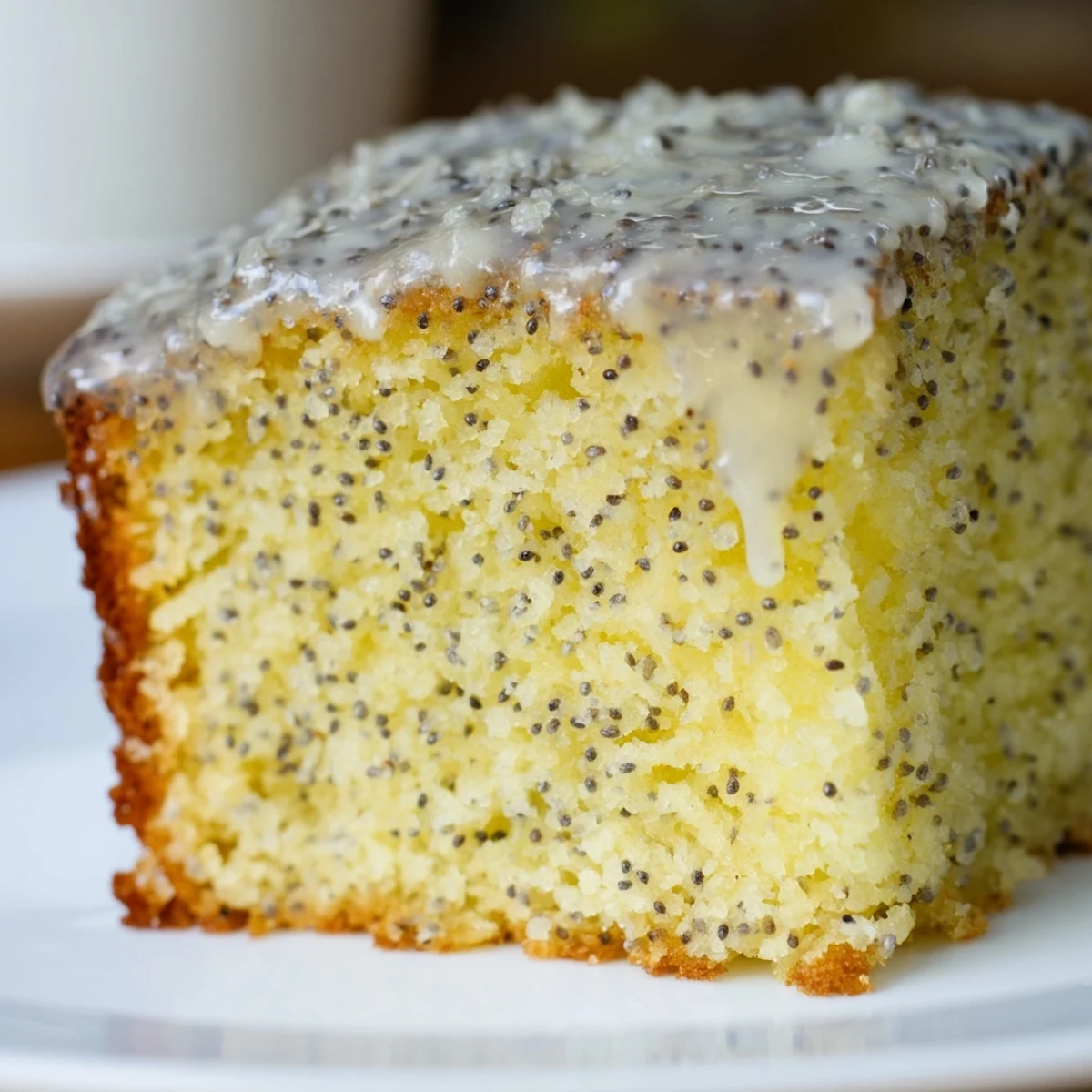 Sliced squares of Lemon Drizzle Traybake with Poppy Seeds, served on a white plate next to a cup of hot Earl Grey tea.