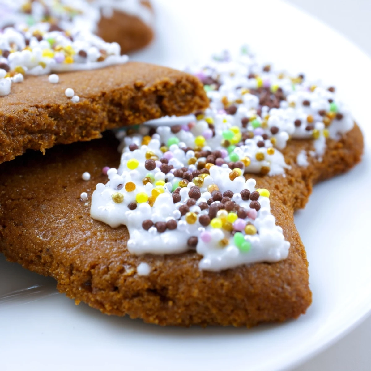 Warm Gingerbread Cookies with Spice iced with white royal icing and stacked neatly on a holiday plate.