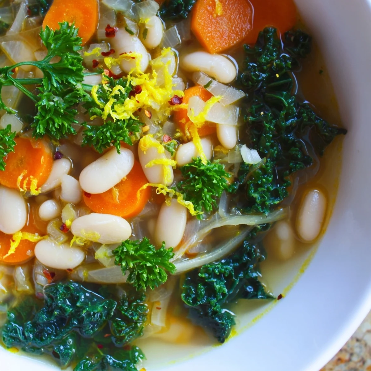 A steaming bowl of White Bean and Kale Soup with Lemon Zest, featuring tender beans and vibrant green kale, garnished with fresh parsley and served warm.