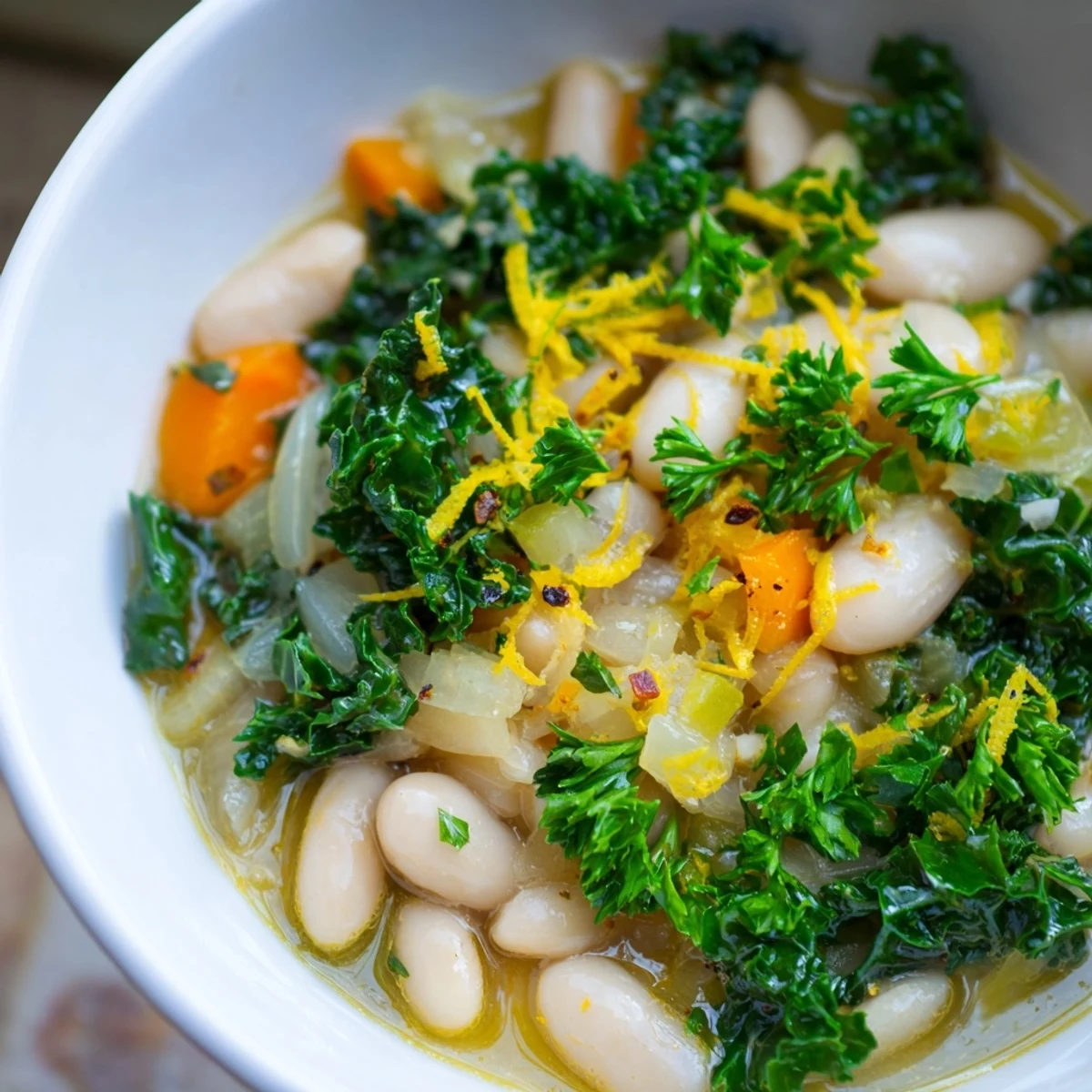 Rustic White Bean and Kale Soup with Lemon Zest served in a dark ceramic bowl, garnished with fresh parsley and lemon slices on the side.