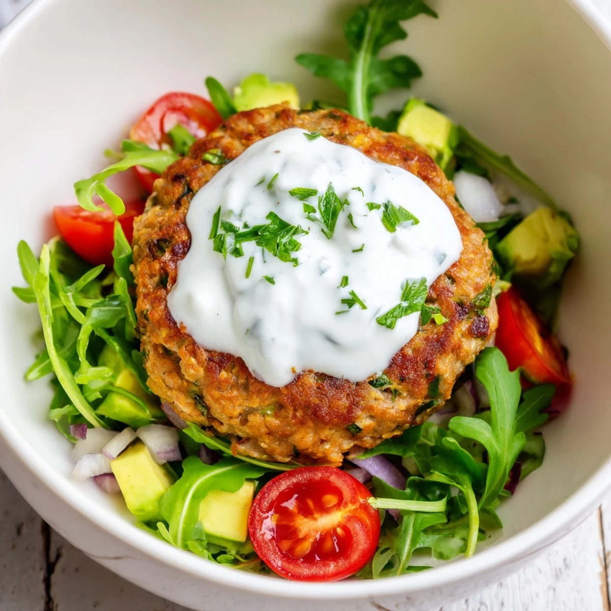 A plated Turkey Burger Salad Bowl with a juicy grilled turkey patty over crisp greens, sliced avocado, and cherry tomatoes, drizzled with creamy yogurt dressing.