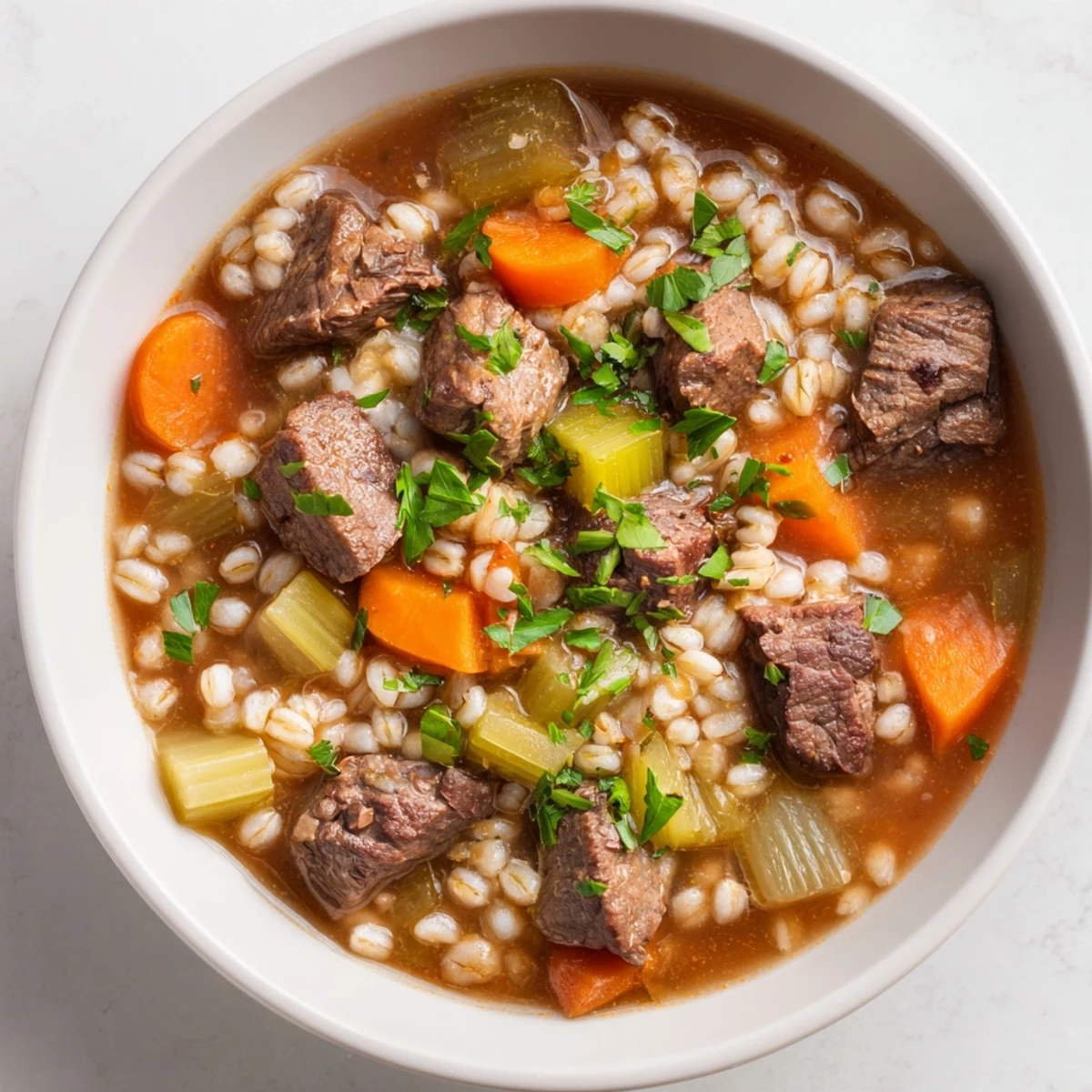 Hearty Beef and Barley Stew with Carrots and Celery simmers in a Dutch oven with fresh herbs.  