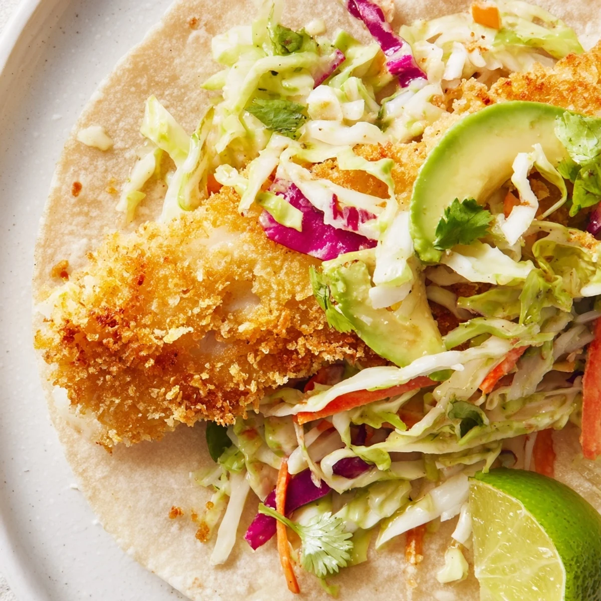 Crispy fish tacos filled with panko-crusted fillets, creamy cabbage slaw, and ripe avocado slices on soft tortillas.