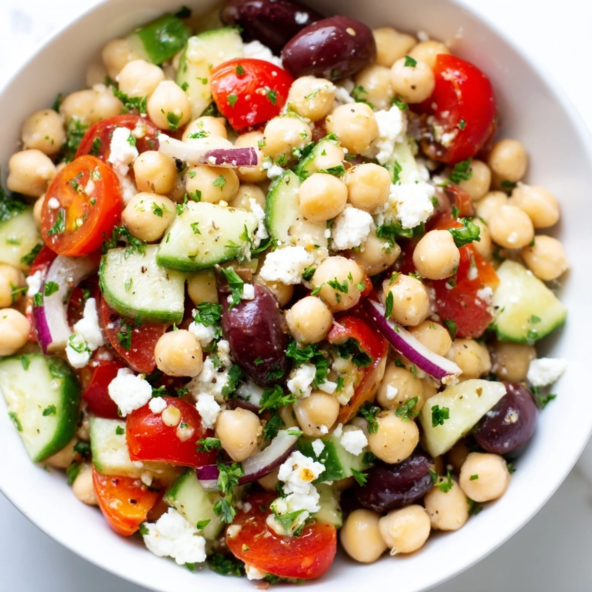 Freshly prepared Mediterranean Chickpea Salad topped with crumbled feta and parsley, served in a white bowl as a healthy side dish.