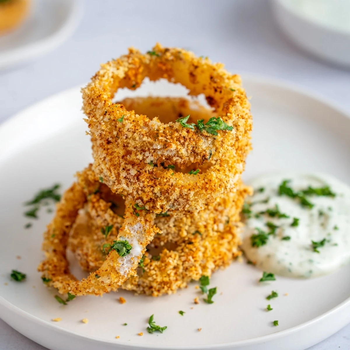 A hand dips a Crispy Baked Onion Ring with Ranch into creamy homemade dressing, highlighting the texture.