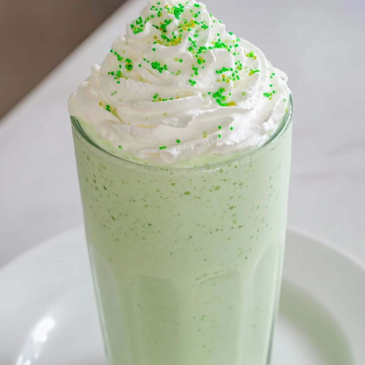 Vibrant green Shamrock Mint Milkshake poured into a straw-ready glass, evoking cool, sweet mint flavors.