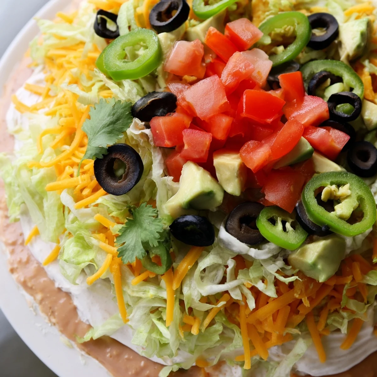 Spicy jalapeños and shredded cheese top the Ultimate Layered Taco Dip, served with a heaping bowl of chips.