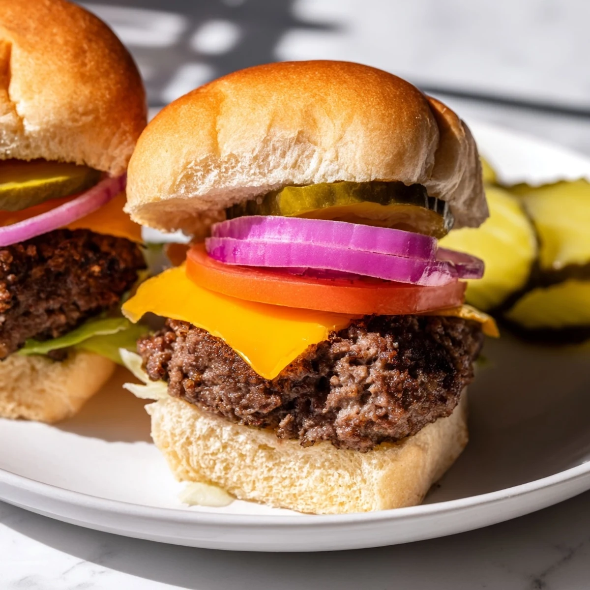 Juicy mini beef burgers topped with gooey cheddar, pickles, and onion on toasted buns, served on a rustic wooden board.  