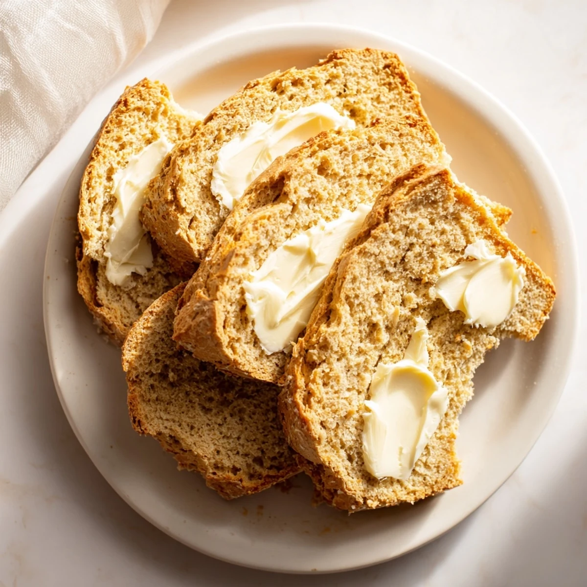 Golden-brown Irish soda bread with a deep cross on top rests on a wooden board beside creamy Irish butter.