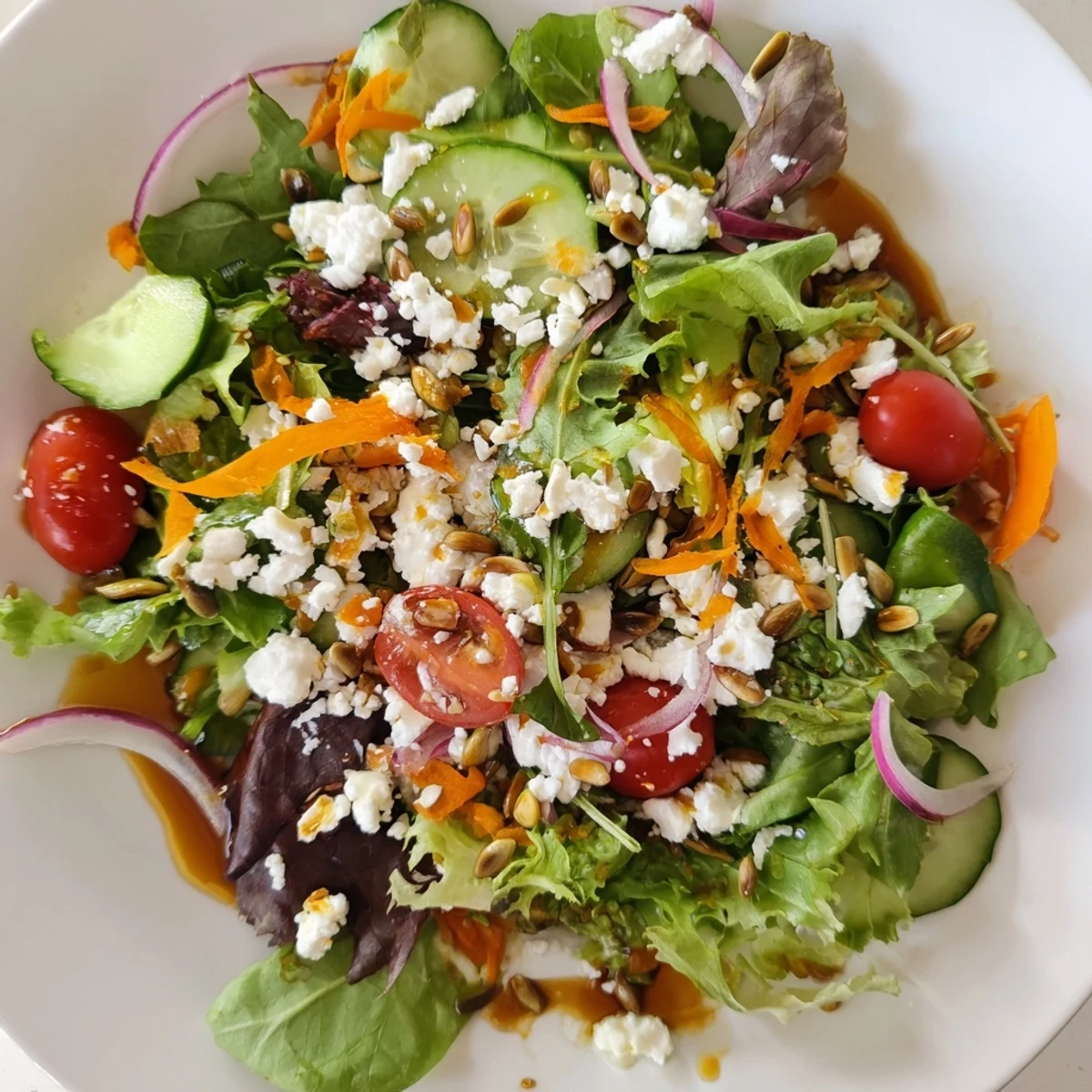 Spring Mix Salad with Vinaigrette drizzled over tender greens, carrots, and sunflower seeds on a rustic wooden serving board.