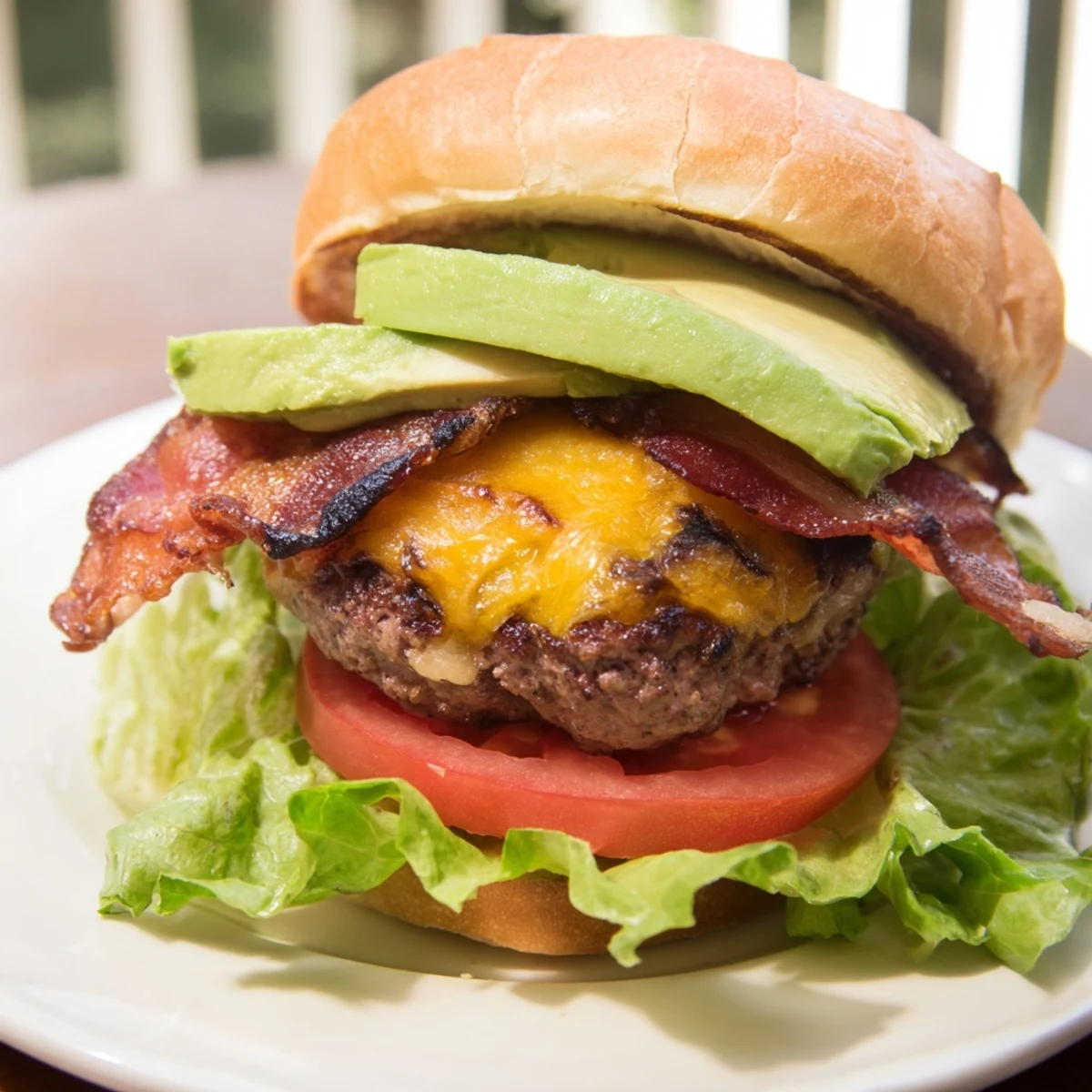 Melted cheddar cheese on a grilled beef patty topped with bacon and avocado slices, ready to be enjoyed for lunch or dinner.