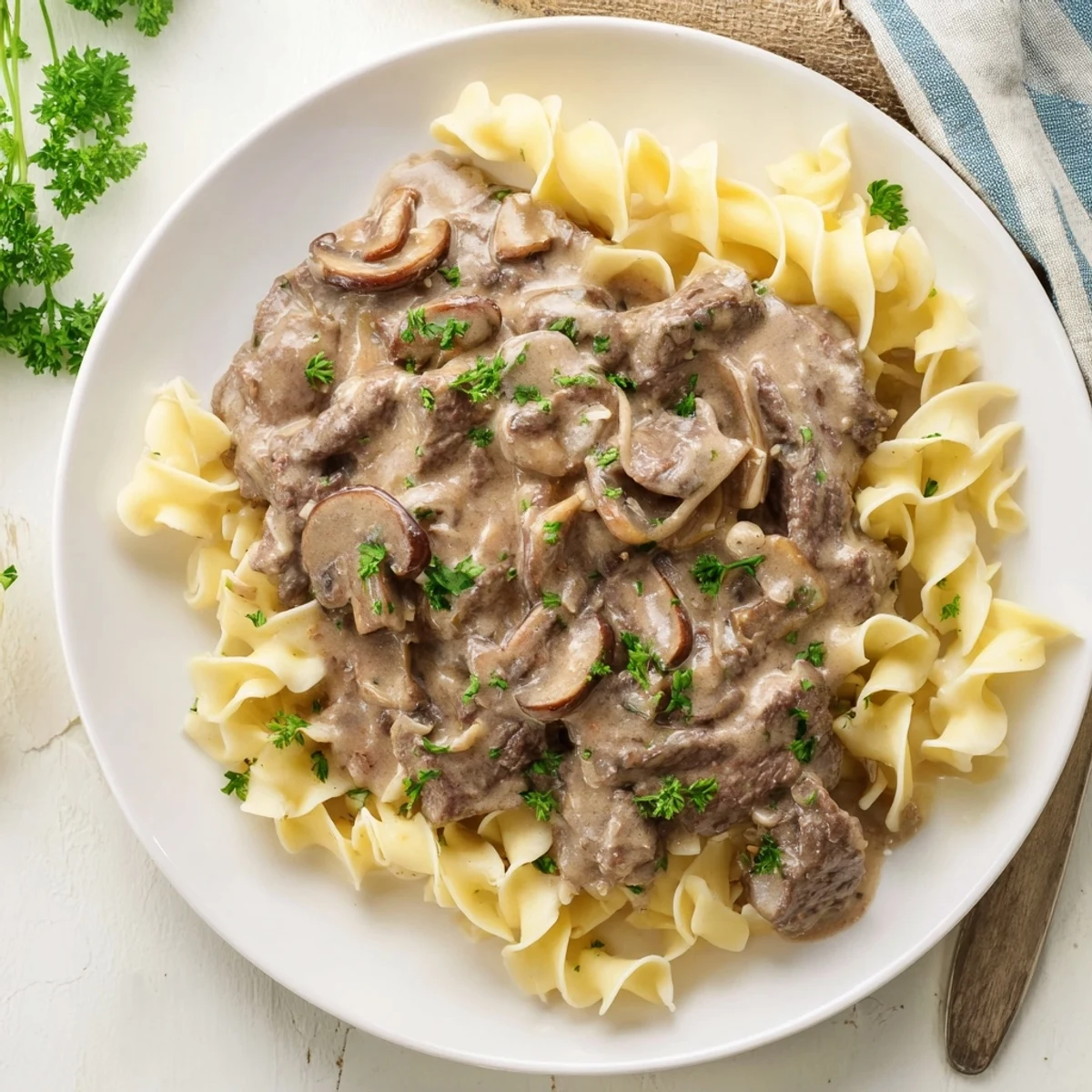 Steaming hot Beef Stroganoff with Egg Noodles featuring rich mushroom gravy, tender beef, and fresh parsley garnish on a white plate.