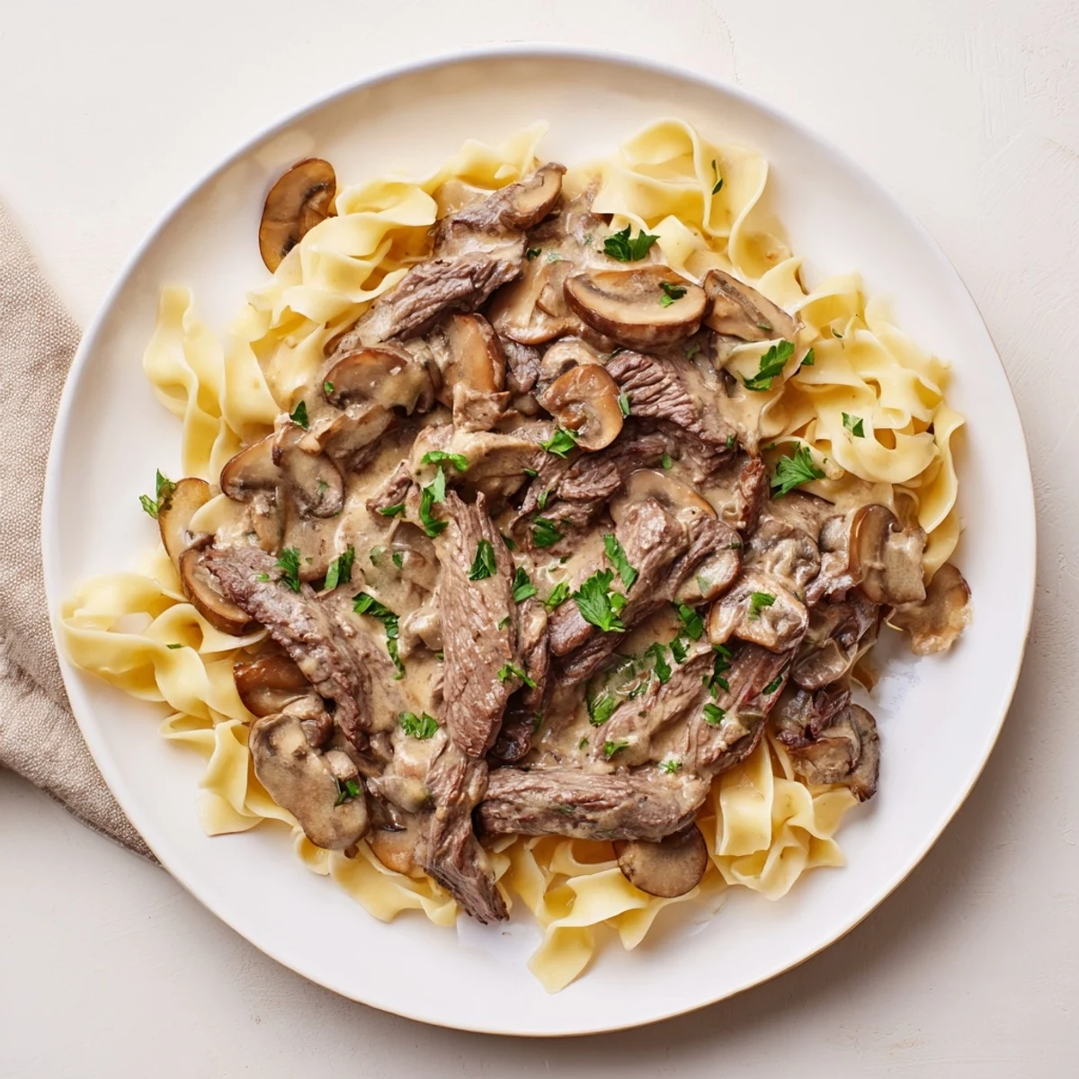 Golden-brown slices of tender beef and sautéed mushrooms coated in a creamy sauce, served over a mound of buttery egg noodles.