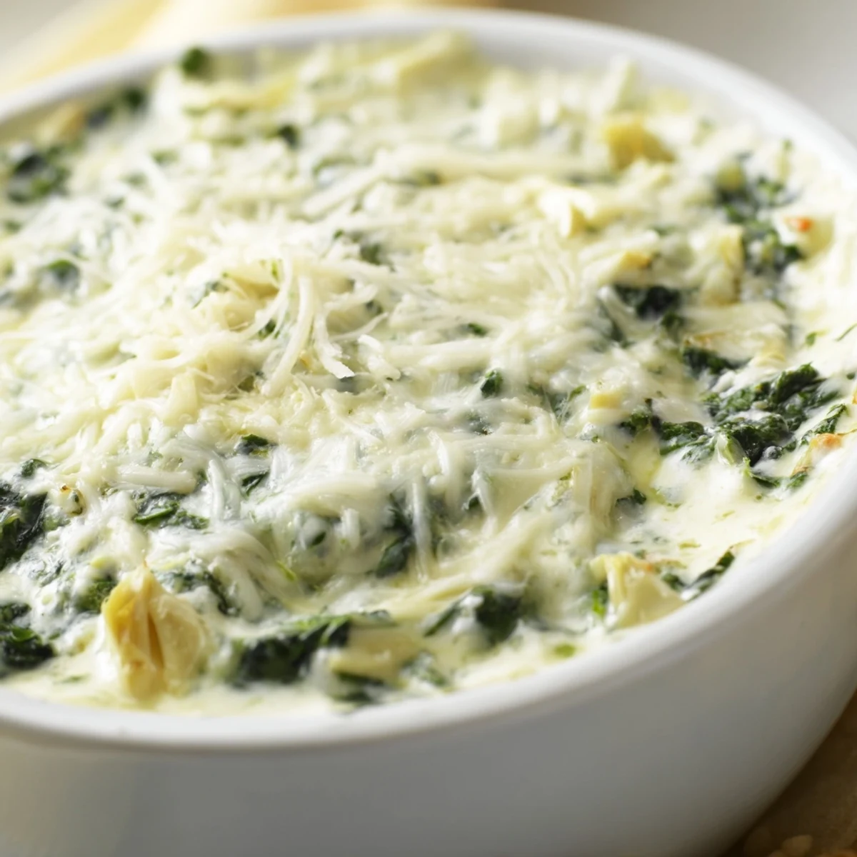 A close-up of golden-bubbly Creamy Spinach and Artichoke Dip with Chips in a ceramic dish.