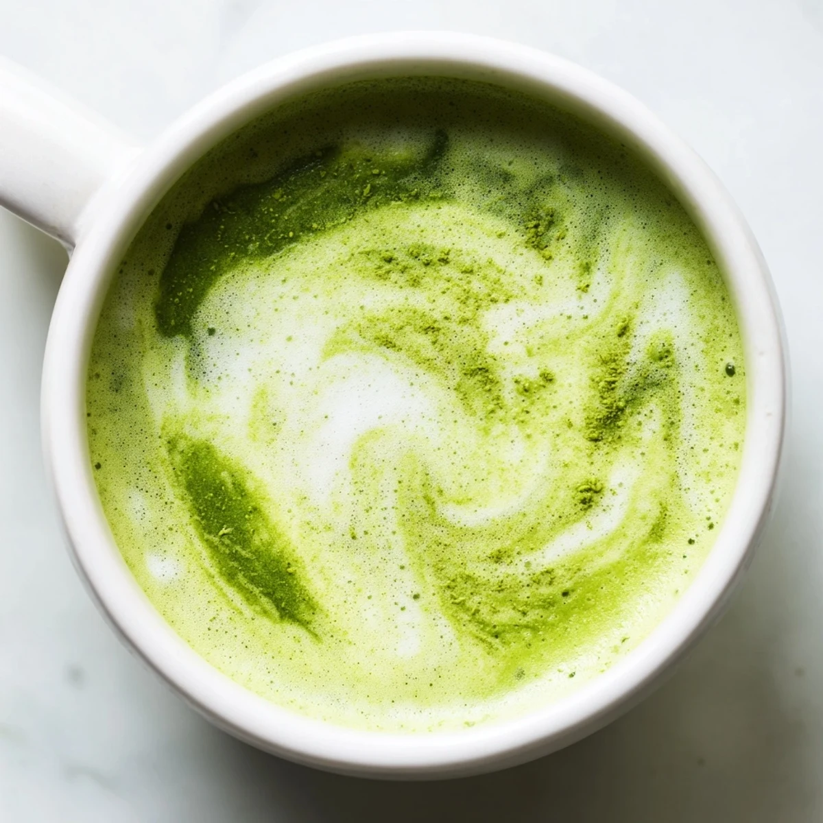 A frothy Green Matcha Latte with Almond Milk is poured into a clear glass mug, showcasing its vibrant green color and creamy almond texture.