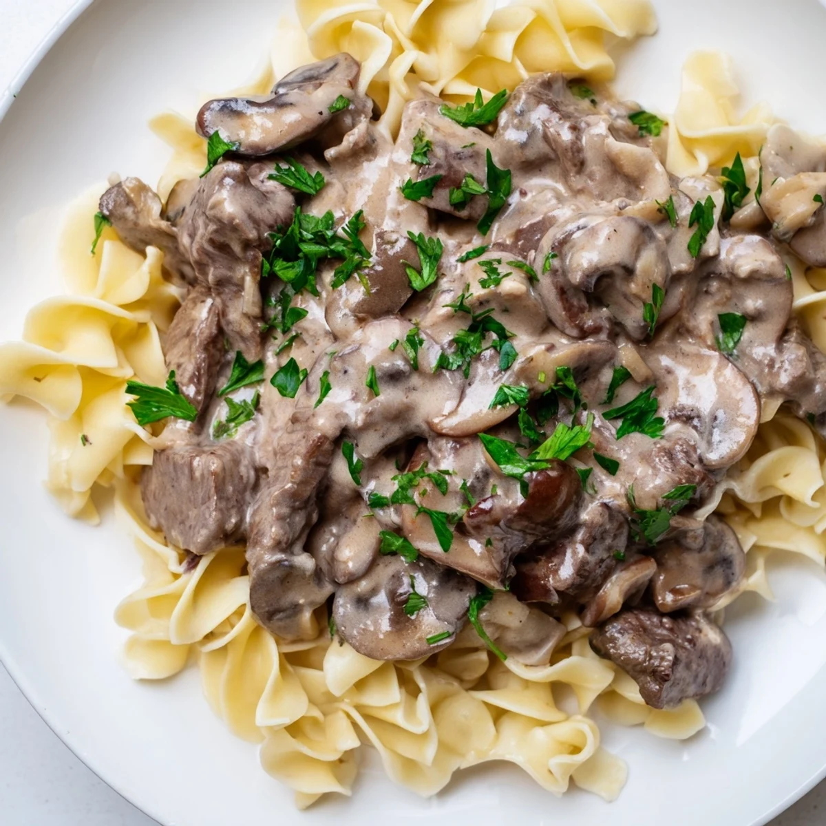Steaming beef stroganoff with egg noodles in a creamy mushroom sauce, garnished with fresh parsley.
