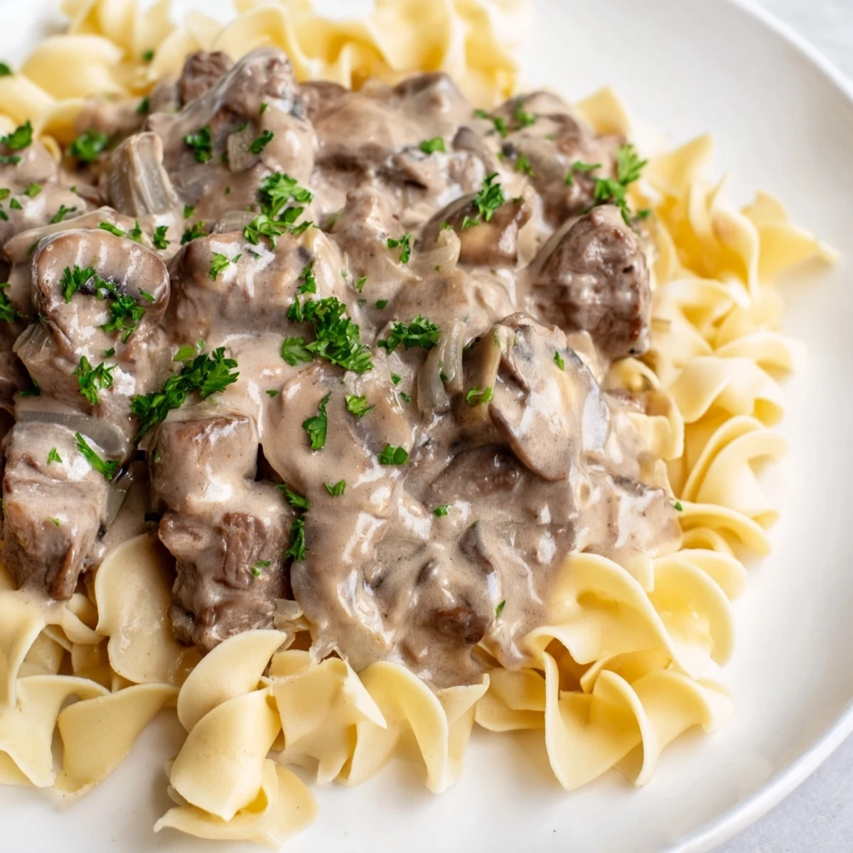 Close-up of tender beef stroganoff with egg noodles on a plate, with a fork ready to serve.