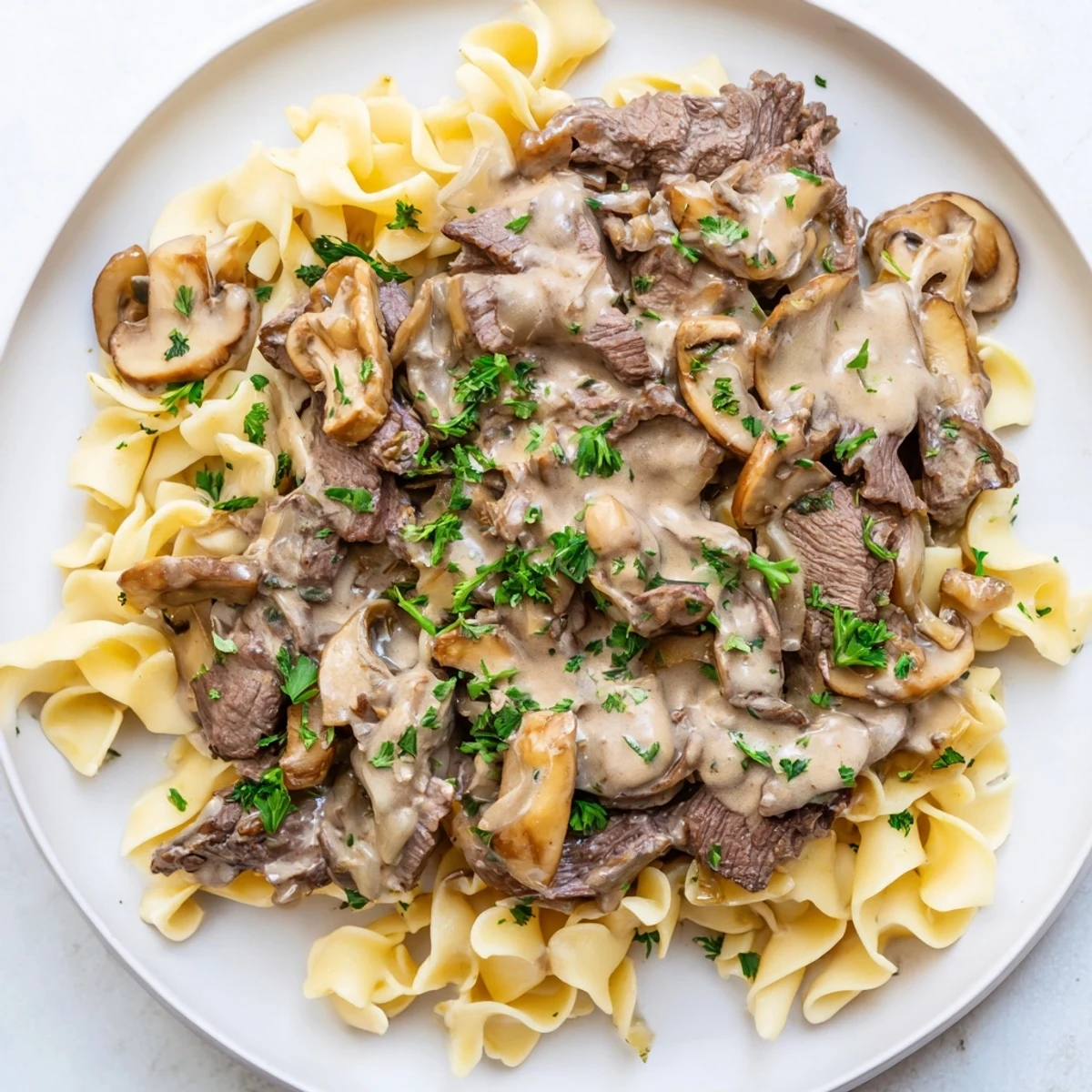 A hearty bowl of Beef Stroganoff with egg noodles, featuring savory flavors and garnished with fresh green parsley.
