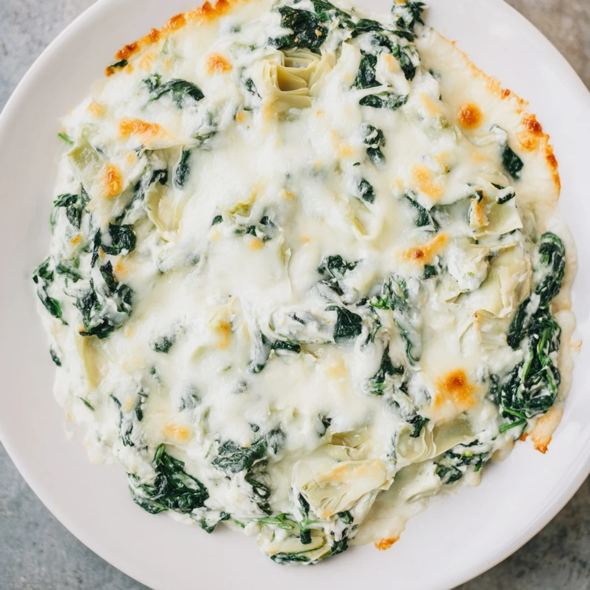A golden-baked creamy spinach and artichoke dip bubbling in a dish, ready to scoop with a crusty bread slice.