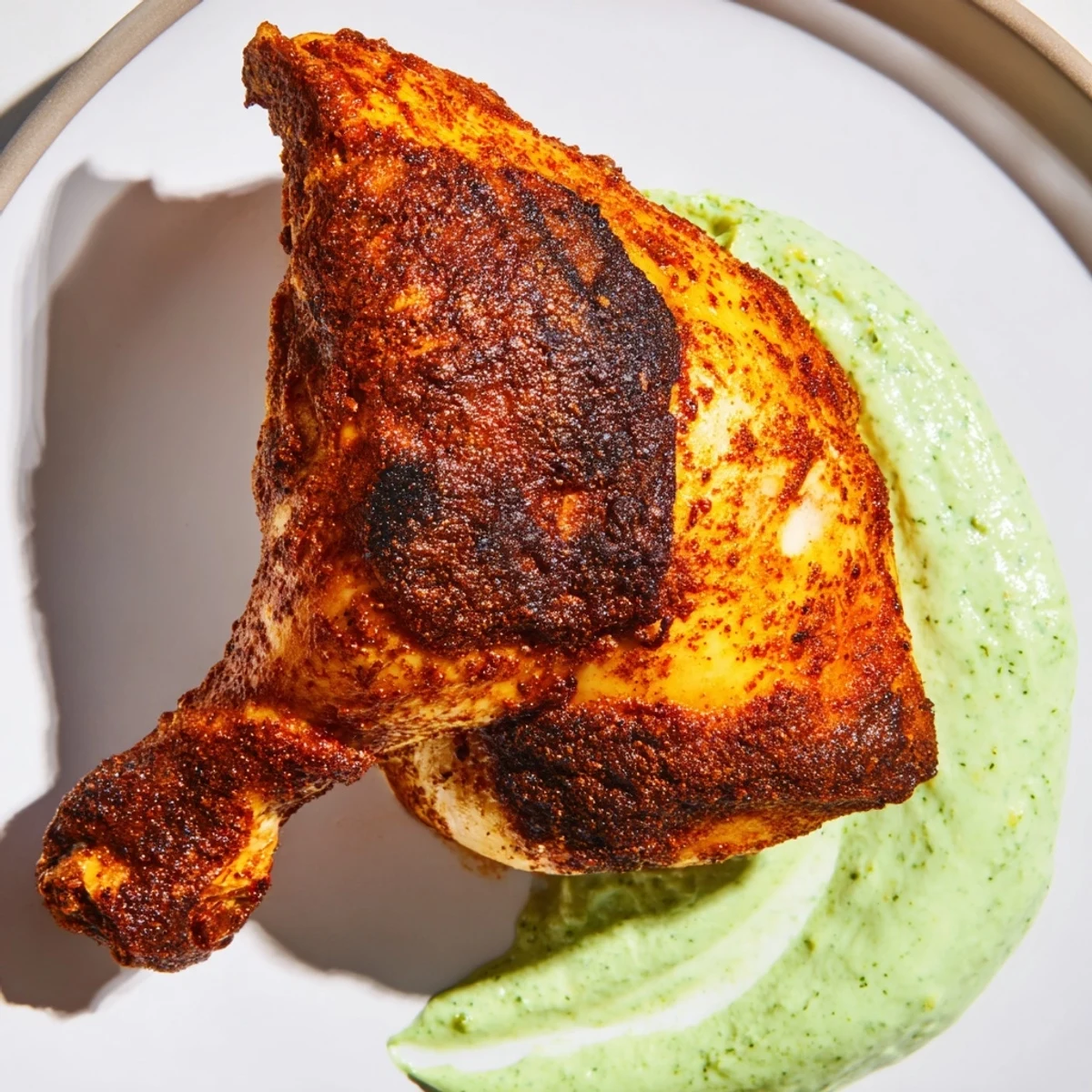 Juicy Peruvian Roast Chicken with Creamy Green Sauce is plated beside roasted potatoes and fresh lime wedges.