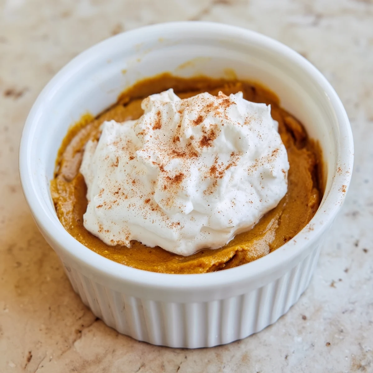 A creamy slice of Effortless Baked Pumpkin Pudding topped with whipped cream and a sprinkle of cinnamon.