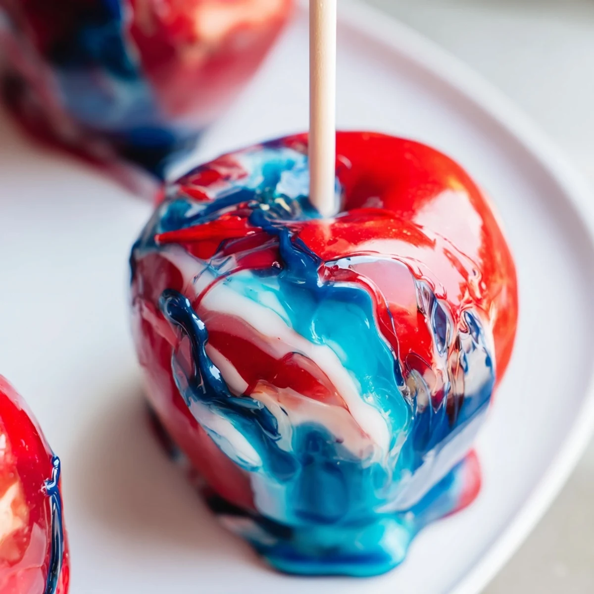 A close-up of marbled effect candy apples with a glossy, swirled red, blue, and white candy shell on a festive platter.
