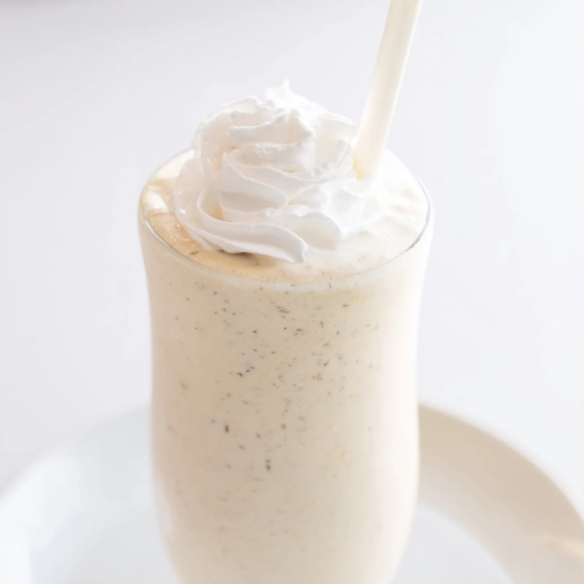 A close-up of Starbucks Vanilla Bean Frappuccino in a tall glass with a swirl of whipped cream on top.