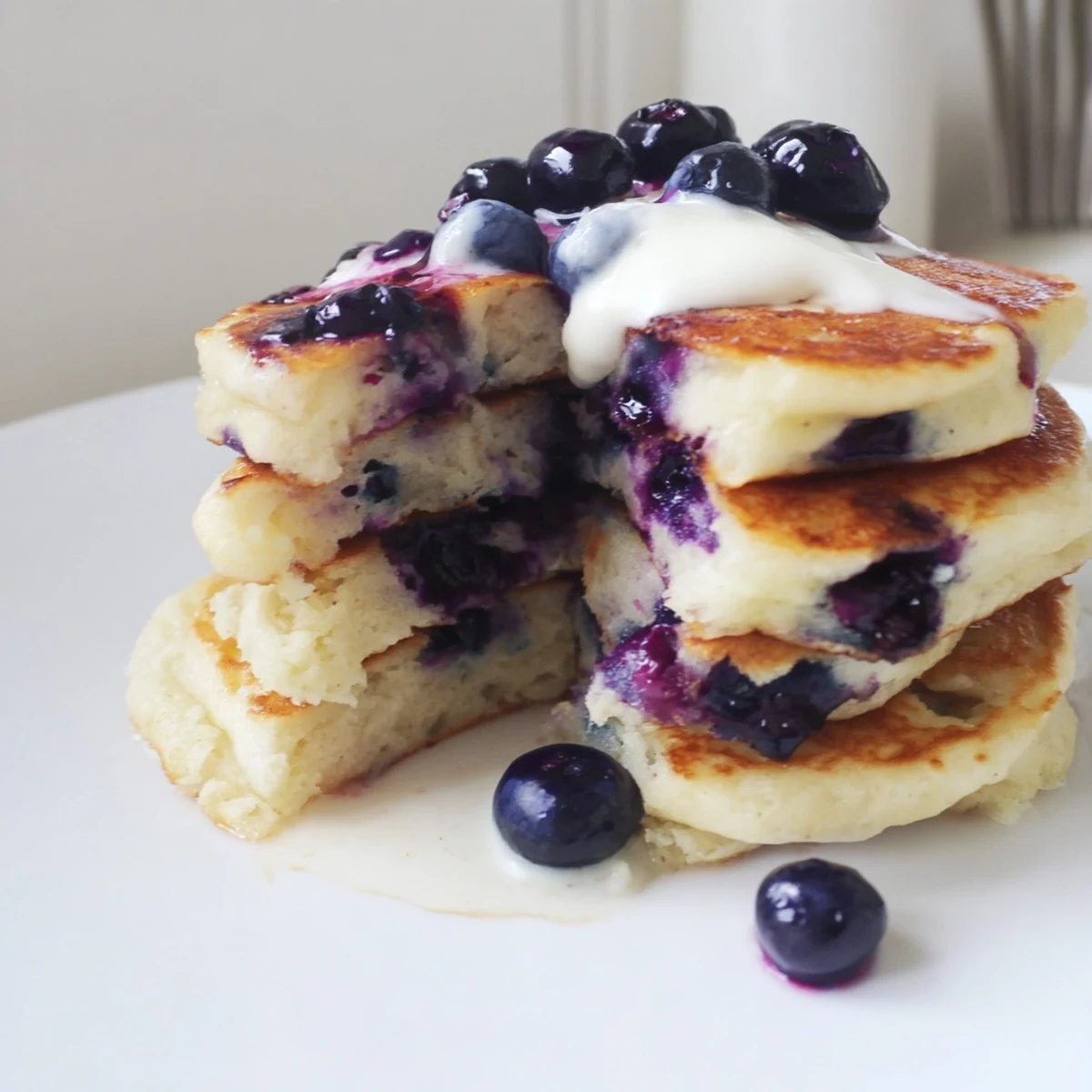 Fluffy Greek Yogurt Blueberry Pancakes stacked high, drizzled with maple syrup on a white plate for a cozy American breakfast.