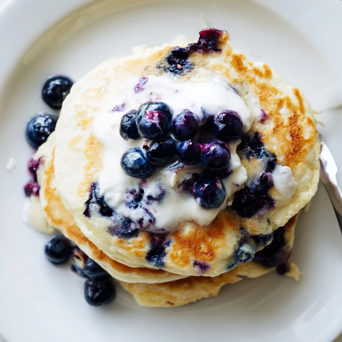 Warm Fluffy Greek Yogurt Blueberry Pancakes sizzling in a skillet, filled with fresh blueberries and served with creamy Greek yogurt dollop.