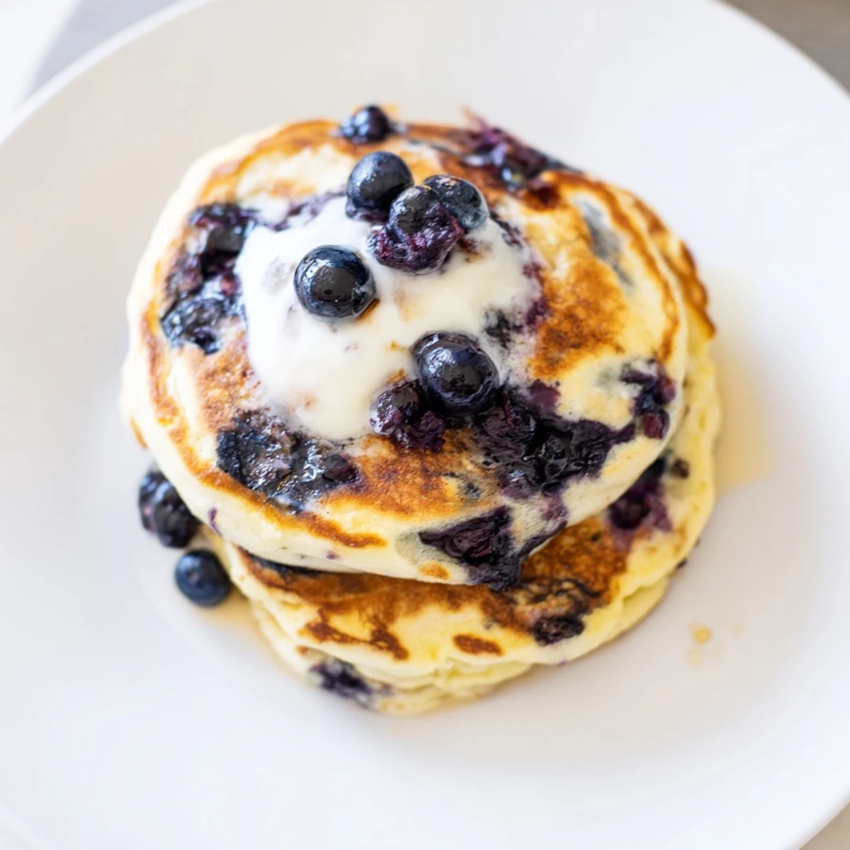Golden Fluffy Greek Yogurt Blueberry Pancakes on a wooden board, topped with syrup and extra blueberries for a healthy brunch meal.