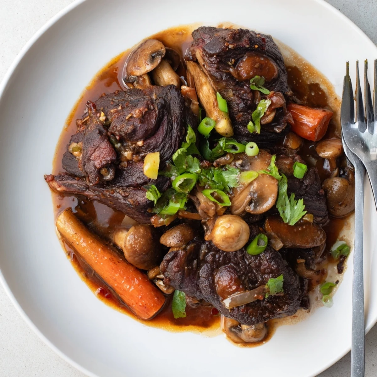 Fork-tender Asian Style Slow Cooked Beef Cheeks With Mushrooms in a rich umami sauce, garnished with fresh cilantro and green onions.