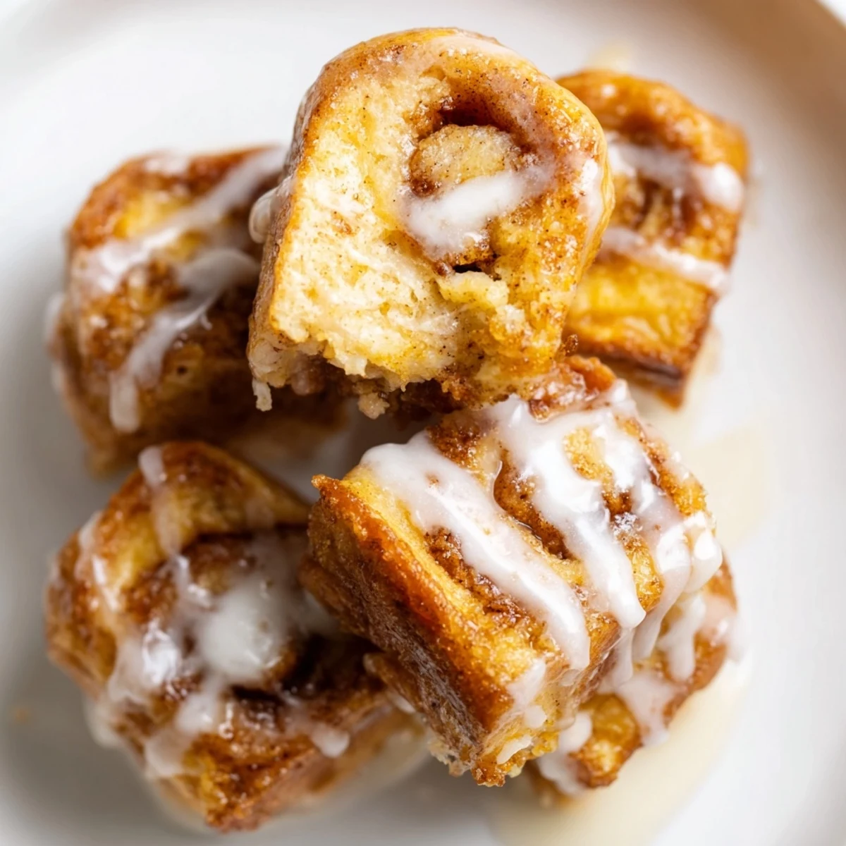 Golden-brown Cinnamon Roll French Toast Bites drizzled with icing and served with fresh berries on a rustic plate.