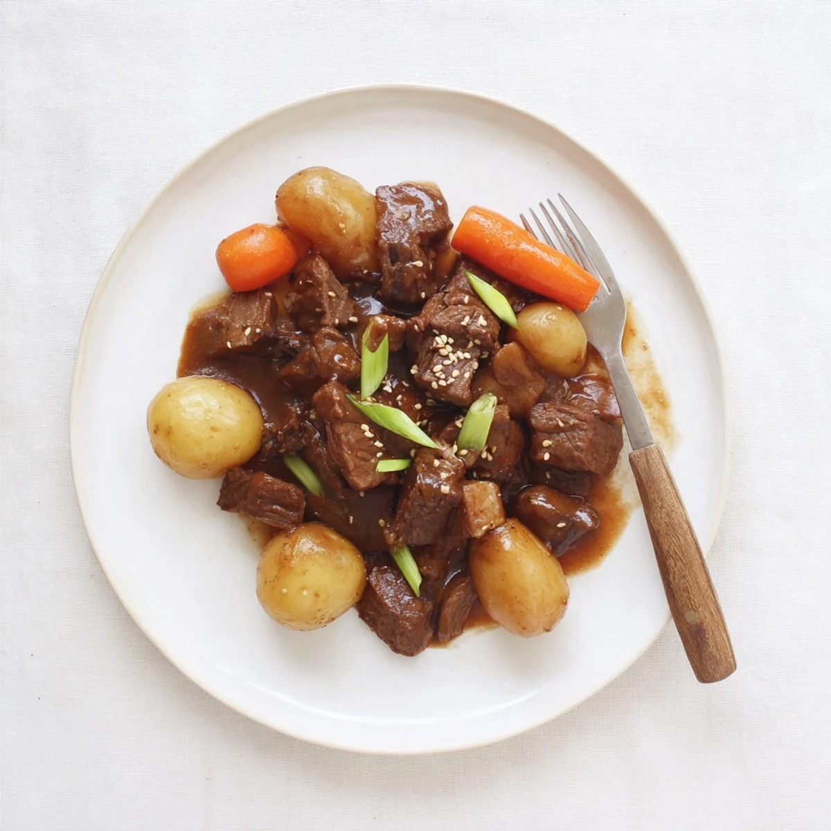 A platter of Slow Cooker Korean Beef Pot Roast With Soy Garlic Gravy, garnished with scallions and steamed rice.