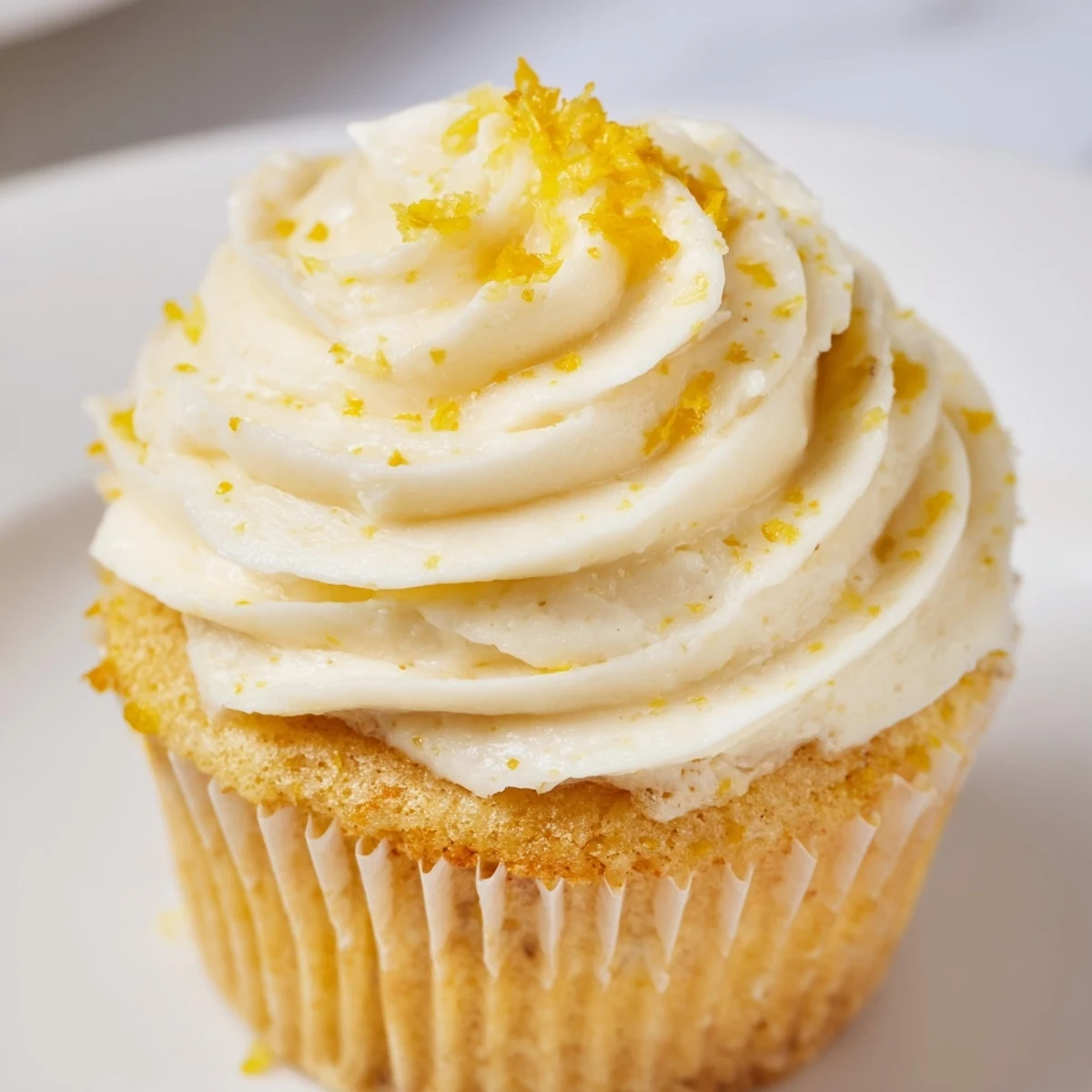 Twelve golden Limoncello Cupcakes rest on a wire cooling rack, showing light moist crumb and creamy Limoncello frosting swirled with lemon zest.  