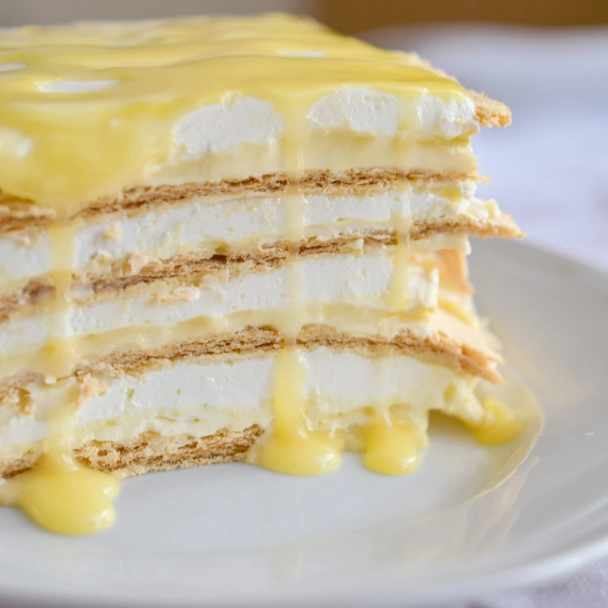 Cool slices of No Bake Lemon Eclair Cake served with fresh raspberries on a white plate at a sunny summer table.