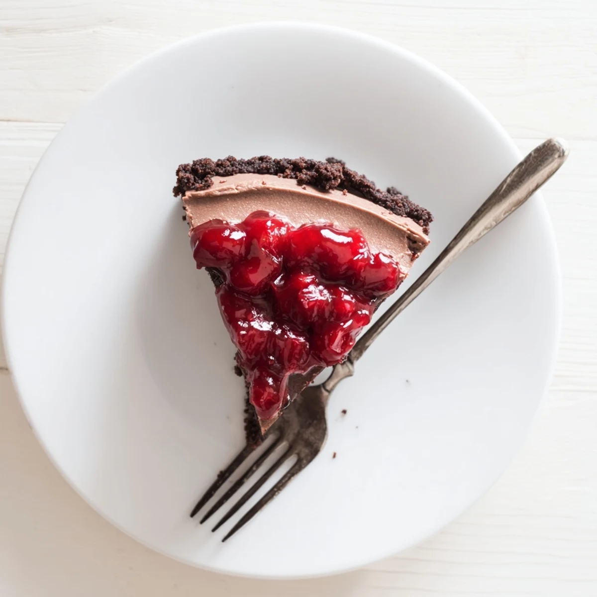 Creamy dark chocolate cherry cheesecake with graham cracker crust and glossy red cherry topping on a white serving plate