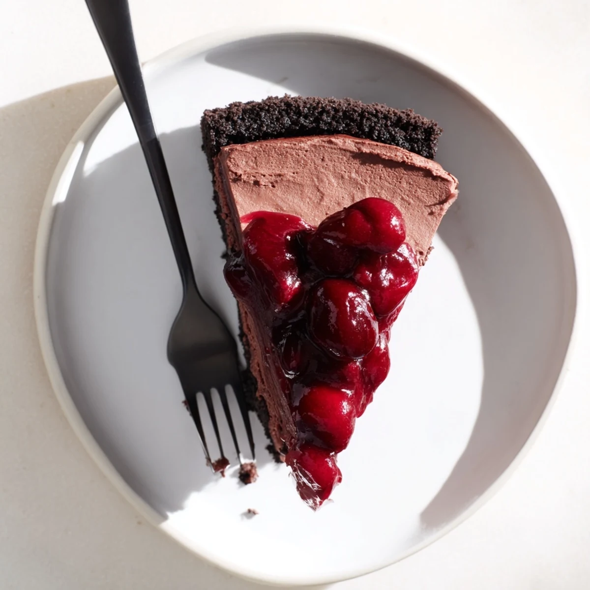 Rich dark chocolate cheesecake slice topped with sweet cherries and dusted with cocoa powder on a marble background