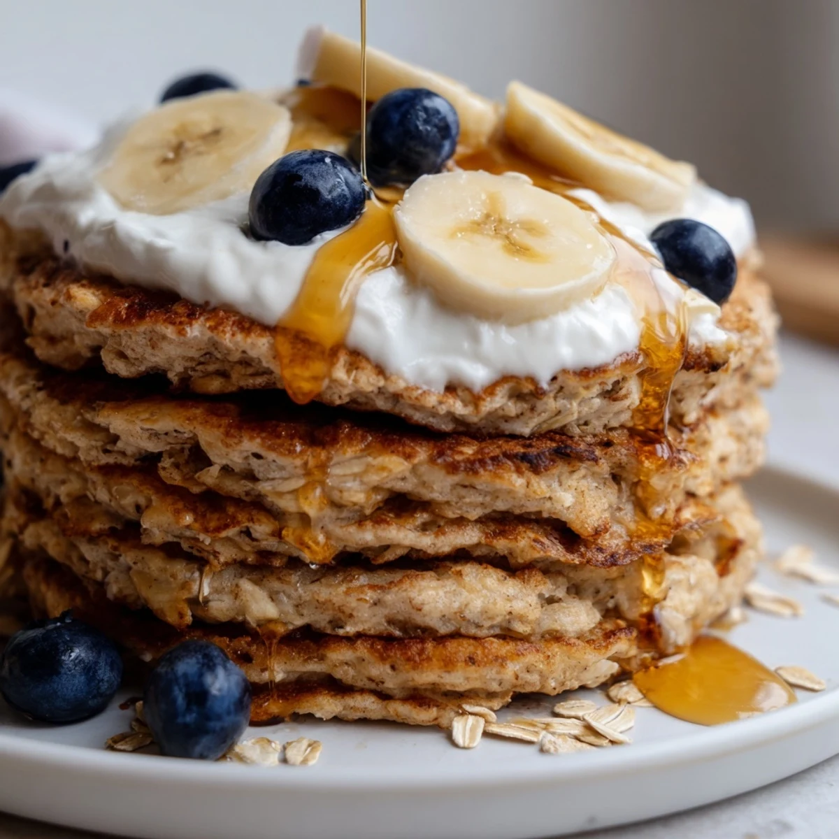 Warm stack of banana oatmeal pancakes drizzled with syrup and creamy Greek yogurt topping
