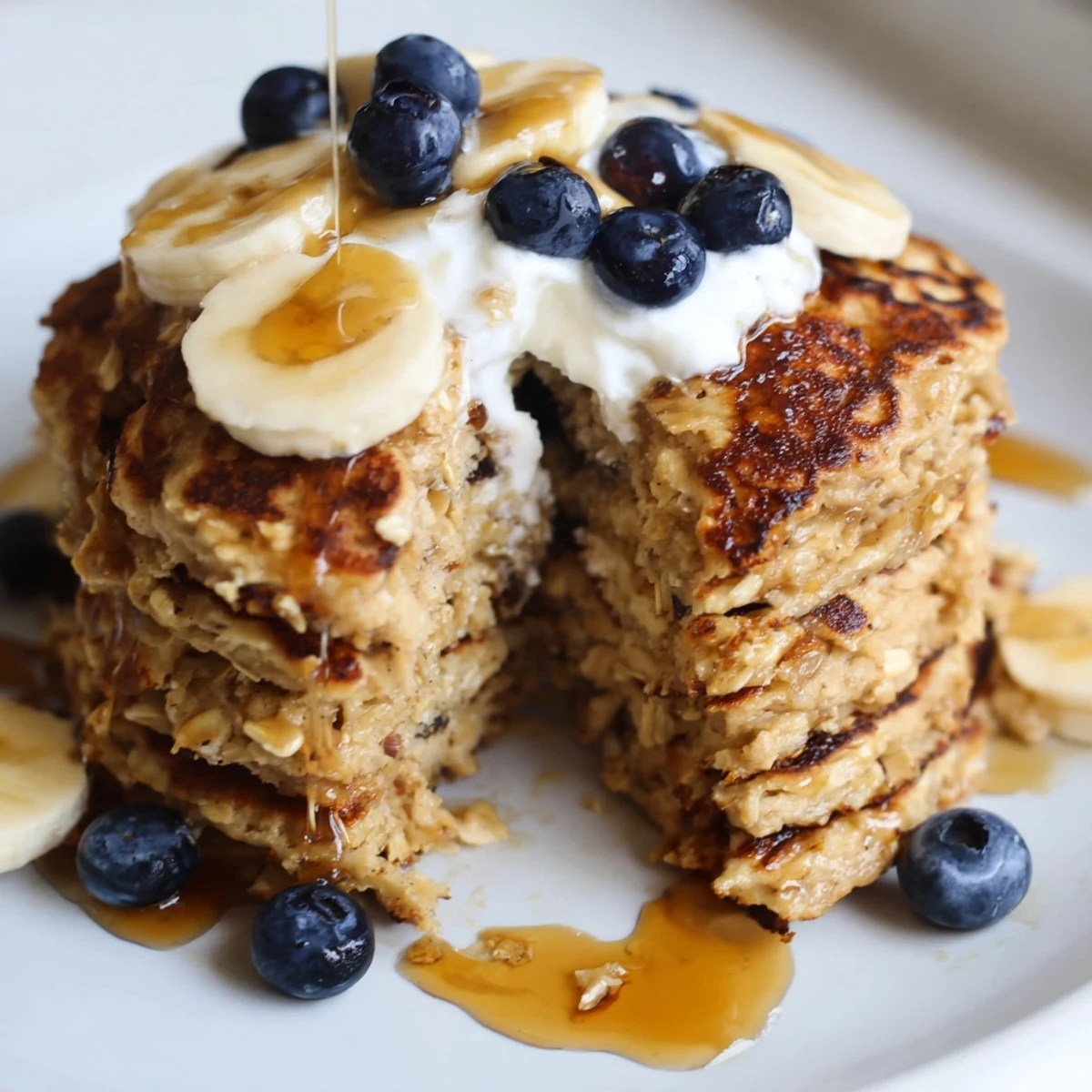 Golden brown banana oatmeal pancakes served with generous dollop of Greek yogurt and maple syrup
