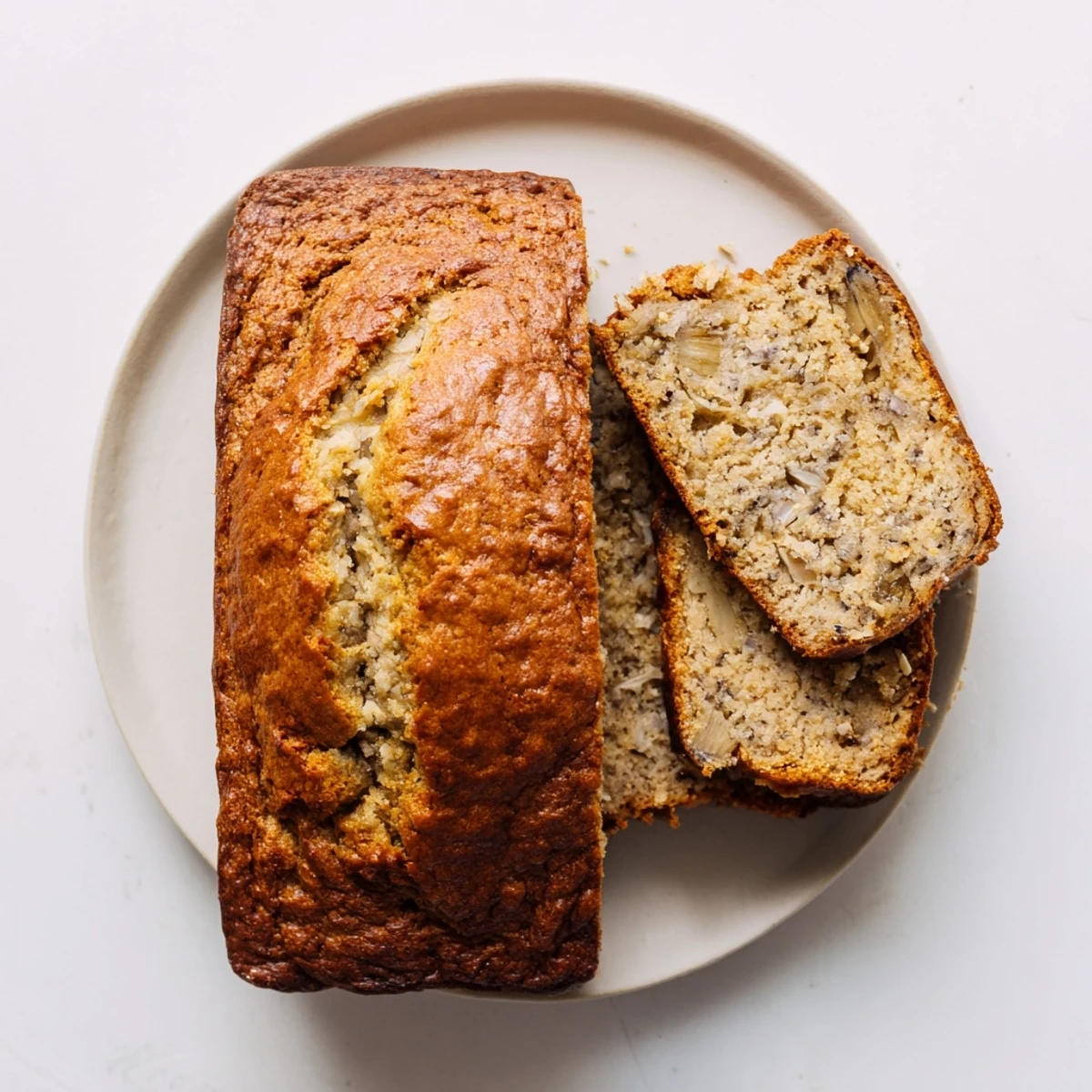 Golden brown moist banana bread loaf sliced on a wooden cutting board with scattered walnuts