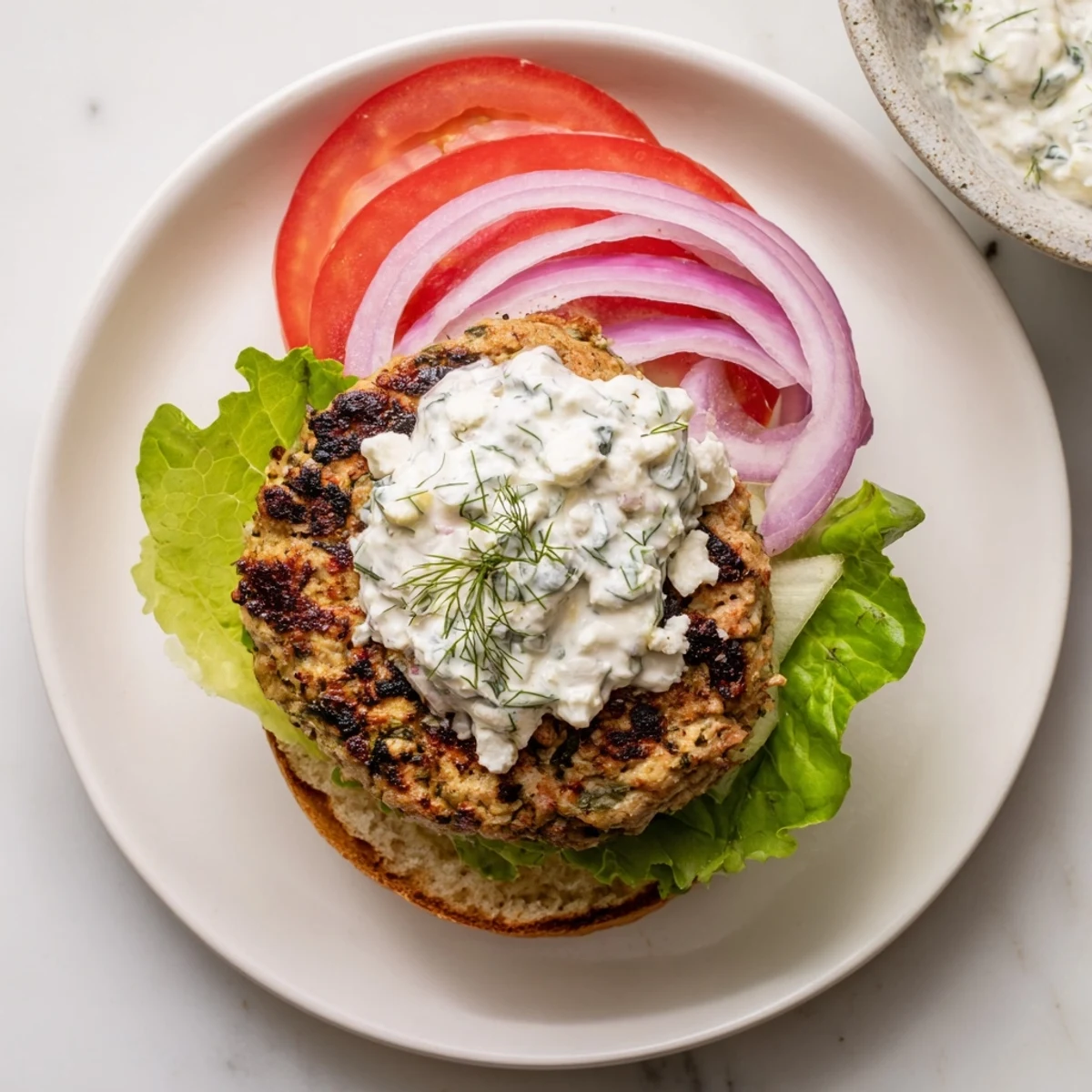 Succulent herb seasoned Greek chicken burgers layered with cool tzatziki, tomato, and crisp red onion
