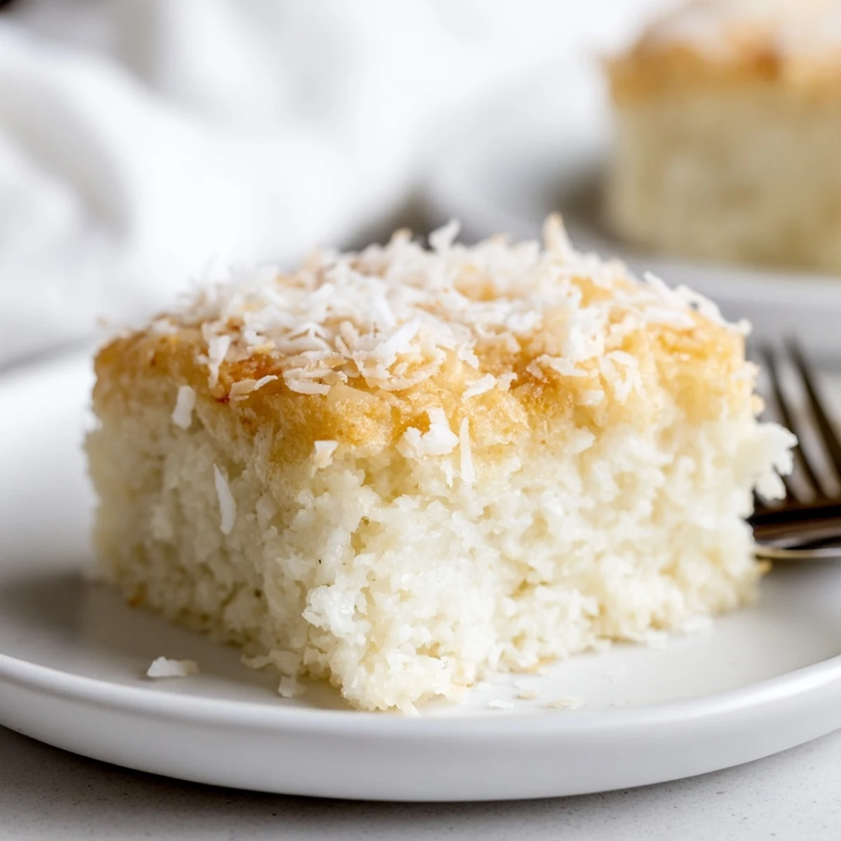 Golden coconut mochi cake squares topped with toasted shredded coconut on a white plate