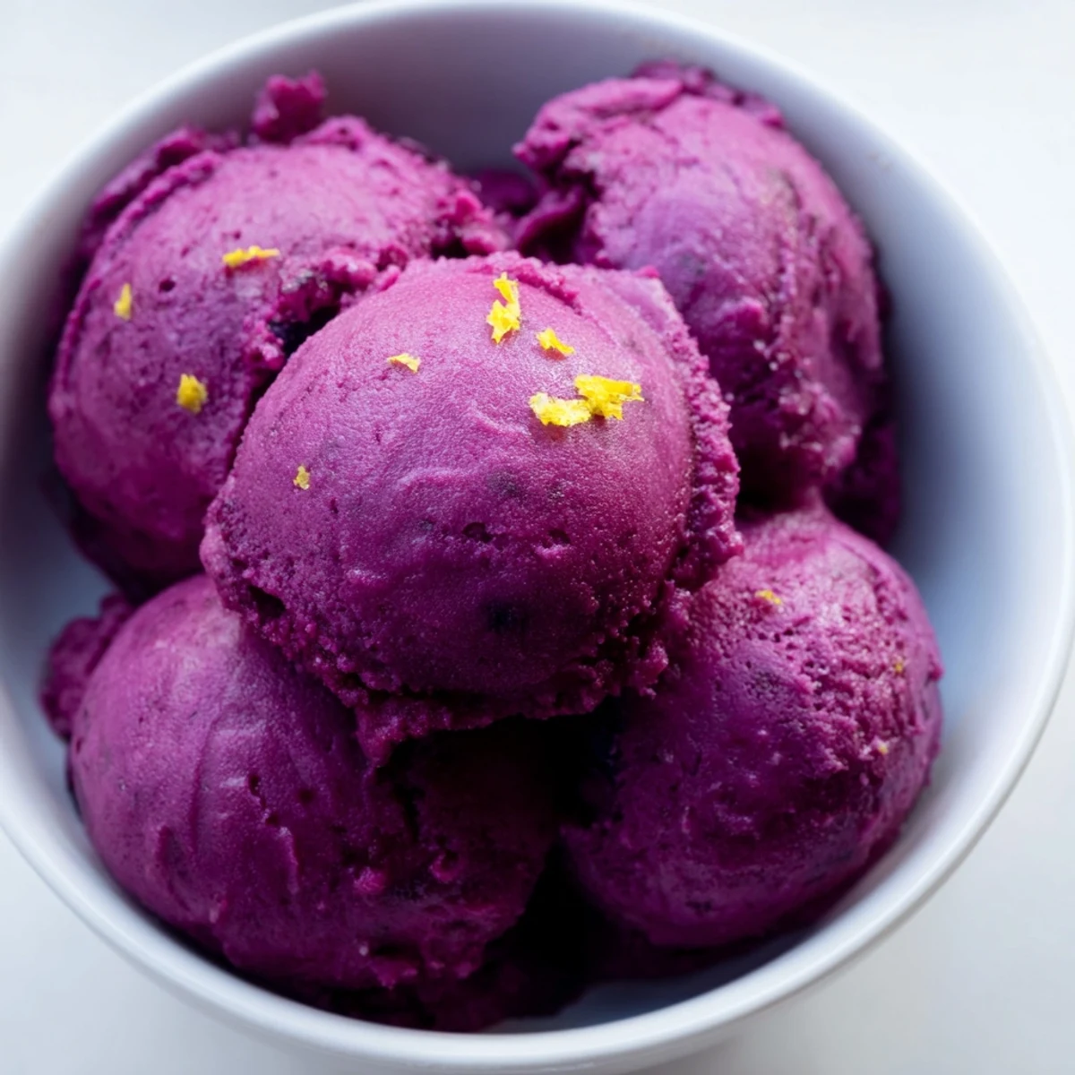 Purple scoop of no churn blueberry lemon sorbet garnished with fresh mint leaves in a chilled glass bowl