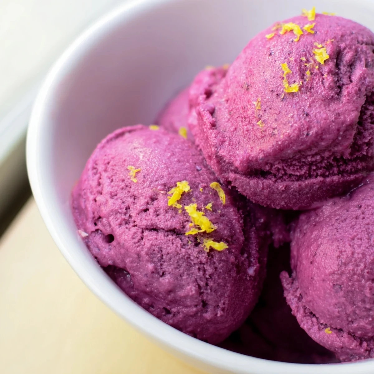 Vibrant magenta no churn blueberry lemon sorbet topped with fresh blueberries and lemon zest on white plate